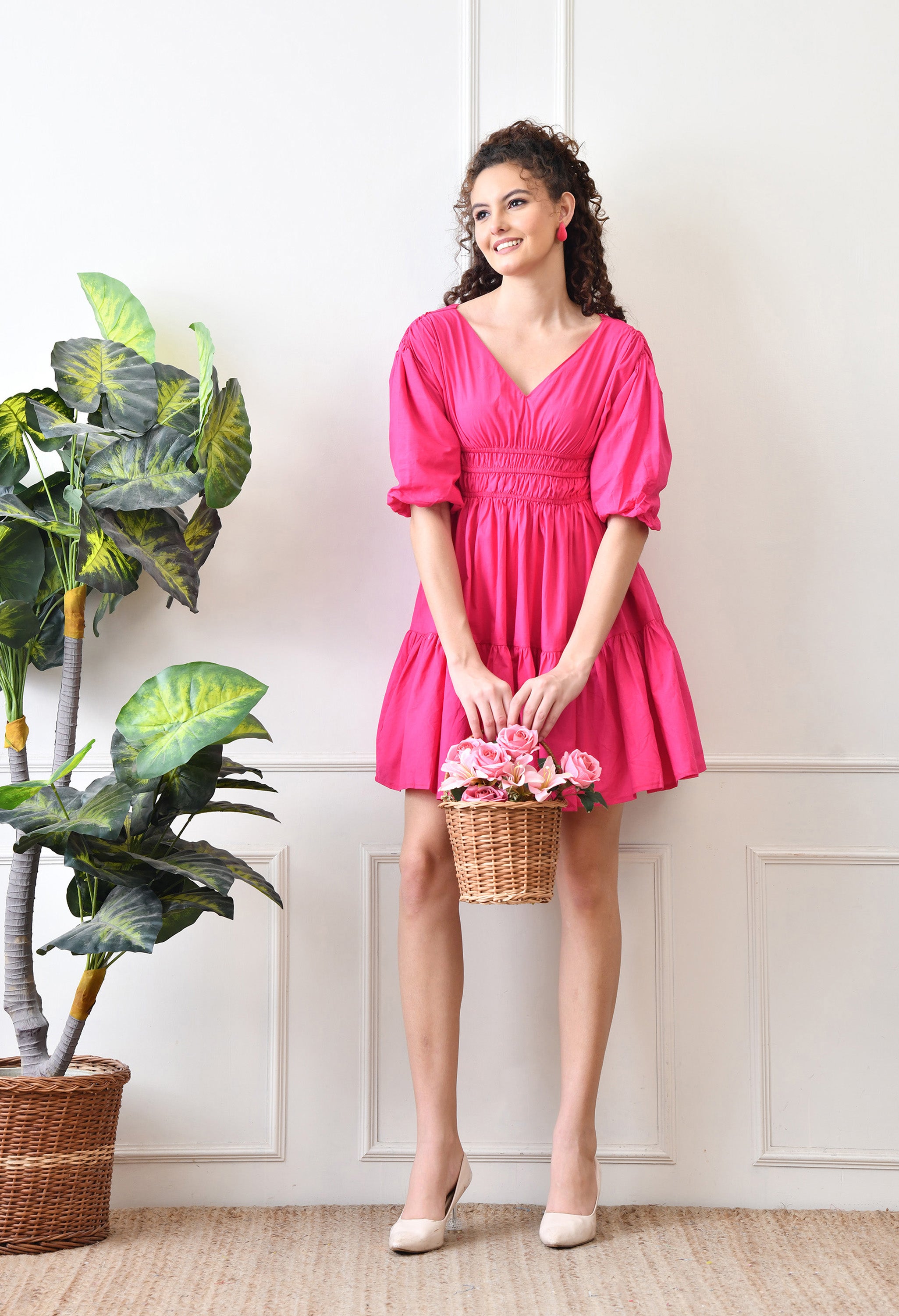 Woman in a pink dress holding flowers indoors with plants and a white wall in the background