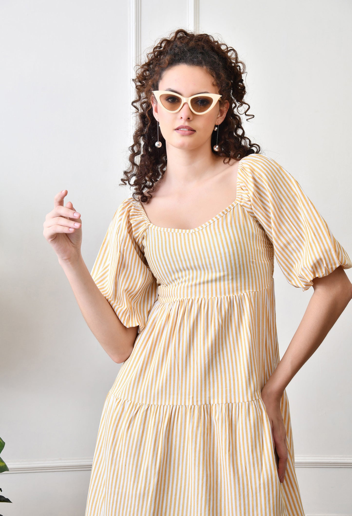 Woman wearing a yellow and white striped dress with sunglasses indoors.
